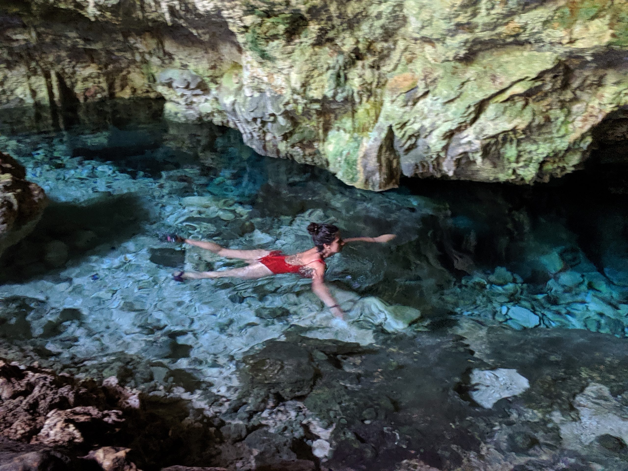 A woman swimming in a pool of crystal clear water in an underground cave